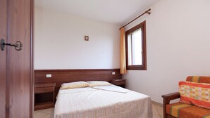 A bedroom with a bed, a wooden nightstand, a chair, a window with curtains, and a door.