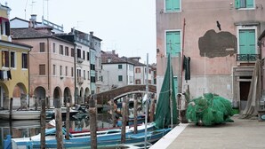A narrow waterway with boats docked on the left, a bridge in the center, and buildings with arched windows on the right.