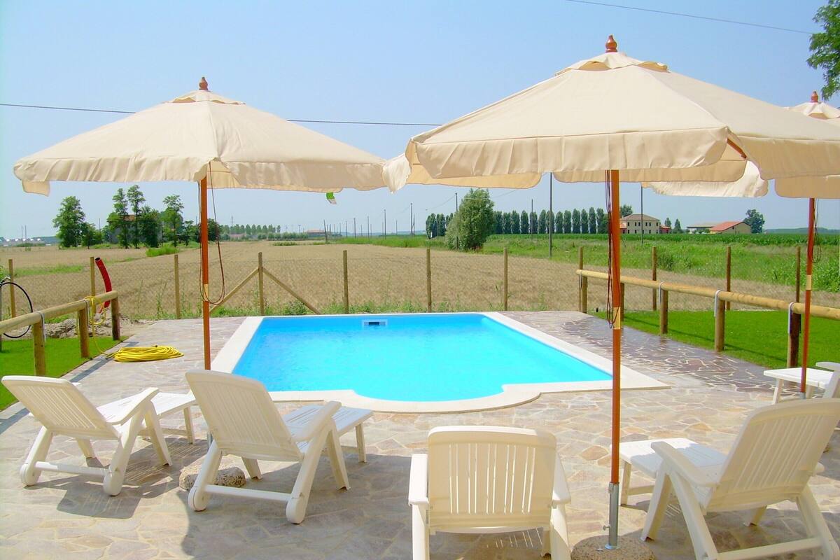 A swimming pool with white chairs and umbrellas, surrounded by a stone patio.