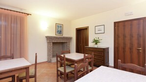 A dining area with a fireplace, wooden furniture, and a door with a plant on a dresser.