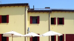 A pool area with white lounge chairs and umbrellas, a clear blue pool, and a yellow building with red shutters.
