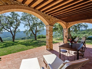 An outdoor patio with stone arches, a table, chairs, and a view of a green landscape. - Farmhouse in Suvereto With Sea Views (Suvereto)