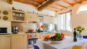 A kitchen with wooden cabinets, a stove, a microwave, and a dining table set with a vase of flowers and a bottle of wine. - Holiday Home in Pascoso Near Forest (Pescaglia)