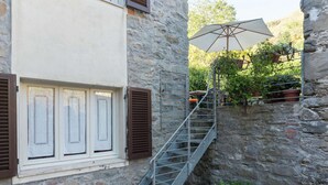 A stone building with a staircase leading to a balcony, a window with shutters, and a large umbrella. - Holiday Home in Pascoso Near Forest (Pescaglia)