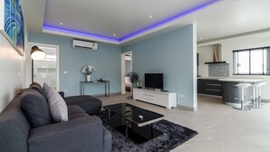 Un salon moderne avec un canapé, une table basse et un téléviseur. Il y a également un coin cuisine avec un bar et une table à manger.
