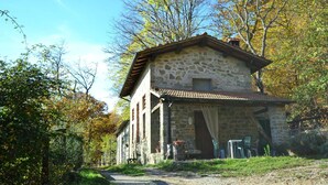 Un bâtiment en pierre avec un toit en tuiles, un porche avec des chaises et un chemin menant à l’entrée.