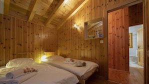 Una camera in baita di legno con due letti, un comodino e una piccola mensola con libri.