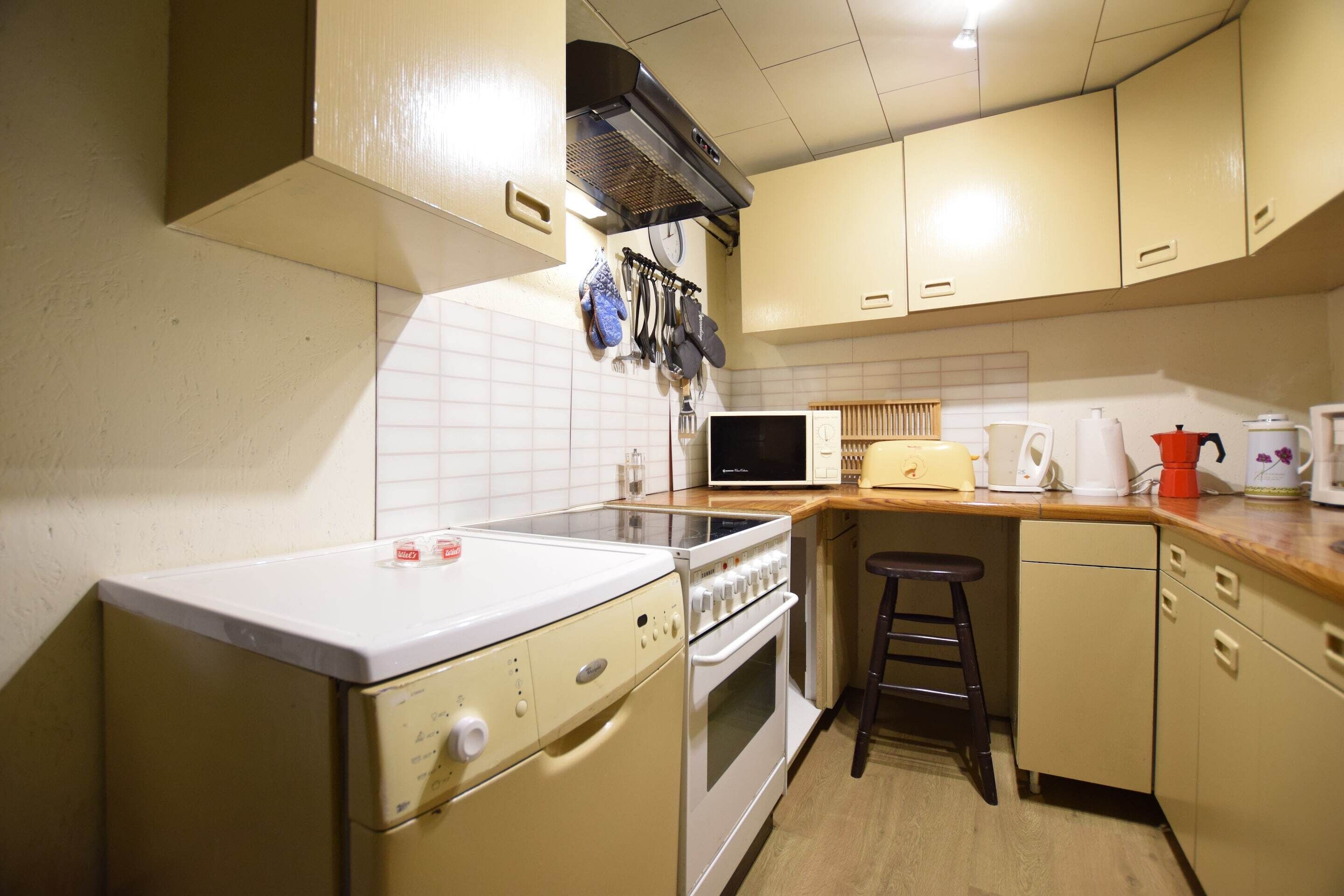 A compact kitchen with a microwave, stove, and oven. There are hanging utensils and a small stool.
