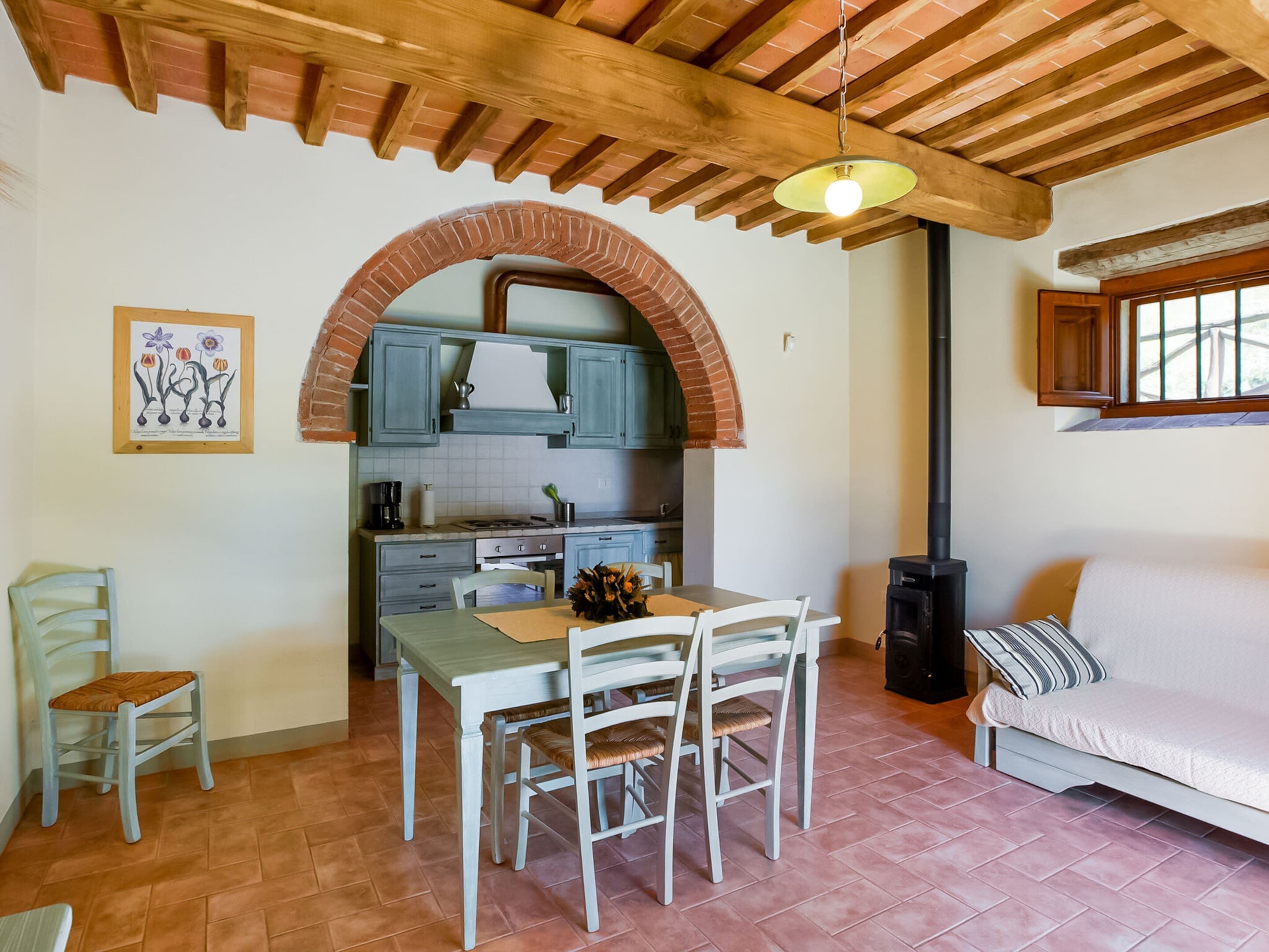 A cozy kitchen with a brick archway, wooden ceiling beams, and a dining area with a table and chairs.