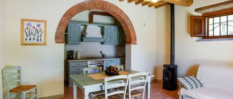 A cozy kitchen with a brick archway, wooden ceiling beams, and a dining area with a table and chairs.