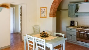 A kitchen with a brick arch, a dining table with chairs, and a hanging light fixture. - Belvilla by Oyo Erica (Anghiari)