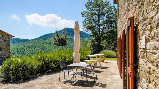 An outdoor patio with stone flooring, a table and chairs, and a view of a mountainous landscape. - Belvilla by Oyo Erica (Anghiari)