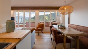 A modern kitchen with a wooden countertop, a dining area with a wooden table and chairs, and a large window with a mountain view. - App. Bellevue B 5.19 (Riddes)