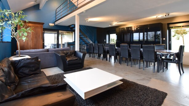 A modern living room with a sofa, coffee table, and dining area. - Luxury Cottage in Vaux-sur-Sûre with Hot Tub (Vaux-sur-Sure)