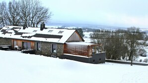A snow-covered house with a stone exterior and a wooden extension. - Luxury Cottage in Vaux-sur-Sûre with Hot Tub (Vaux-sur-Sure)