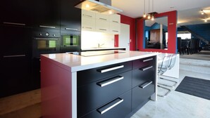 A modern kitchen with black cabinets, a red accent wall, and a stainless steel range hood. - Luxury Cottage in Vaux-sur-Sûre with Hot Tub (Vaux-sur-Sure)