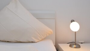 A bed with white bedding and pillows, a bedside table with a lamp, and a white wall. - Wohnung in Willingen Nahe Ettelsberg-bahn (Willingen)