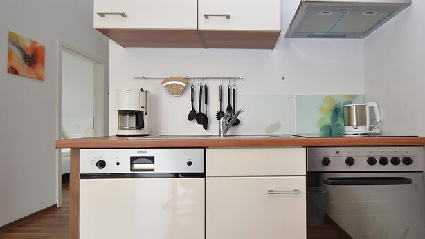 A compact kitchen with white cabinetry, a coffee maker, a kettle, and a stove. - Wohnung in Willingen Nahe Ettelsberg-bahn (Willingen)