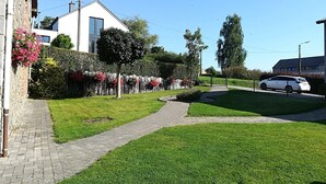 Zona residenziale con un viale lastricato, un'auto bianca parcheggiata in strada e un edificio con un balcone.