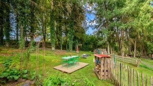 Uma área externa rústica com um deck de madeira, cadeiras de metal verde e uma mesa pequena.