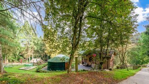 Um cenário rústico ao ar livre com uma tenda verde, estruturas de madeira e um caminho pavimentado.