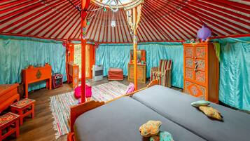 Una yurta tradicional con techo de madera circular, una cama con almohadas coloridas y una pequeña mesa de madera con una silla.