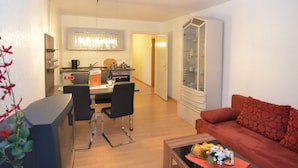 Un salon moderne avec un canapé rouge, un coin repas avec une table et des chaises, et une cuisine agrémentée d’un lustre.