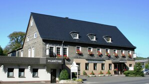 Un bâtiment à deux étages, sur lequel on peut lire les inscriptions « PILSSTUBE » et « RESTAURANT », indiquant qu’il s’agit d’un établissement de restauration.