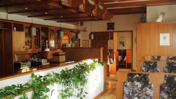 Un restaurant au décor en bois, avec un comptoir et un espace où sont disposées des chaises à motifs.