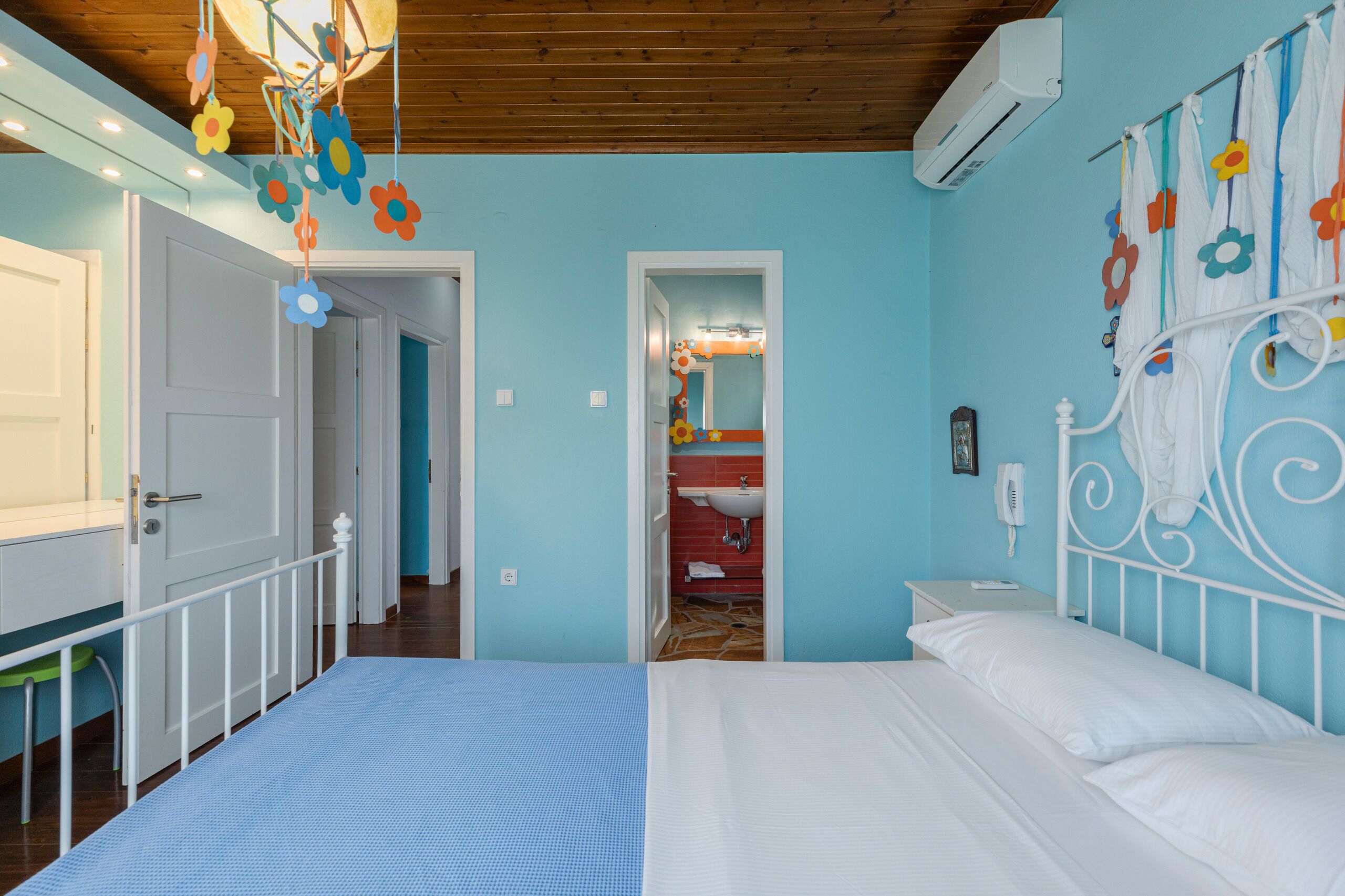 Een slaapkamer met een bed, een wit metalen hoofdbord, een blauwe wand en een houten plafond.