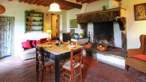A rustic dining area with a wooden table set for two, a fireplace, and a green shelf with kitchenware. - Belvilla by OYO Santa Cecilia (Rufina)