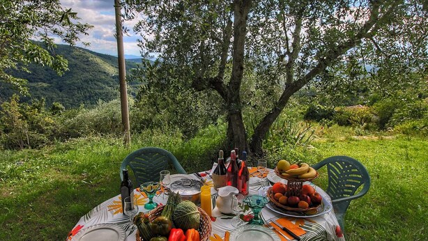An outdoor dining table set up in a lush, green landscape with a view of distant hills. - Belvilla by OYO Santa Cecilia (Rufina)