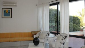 A room with a white sofa, wicker chairs, a small table, and a large window with curtains. - Belvilla by OYO Villa Eirene (Syracuse)