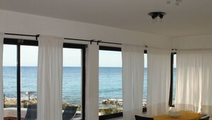 A room with a view of the sea, a dining table with chairs, and a white chair with a cushion. - Belvilla by OYO Villa Eirene (Syracuse)