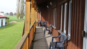 A wooden balcony with a table and chairs, overlooking a grassy area with a building in the background. - Spacious Apartment in Boddin With Garden (Walkendorf)