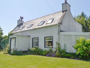 Une maison blanche à deux étages, avec un toit en pente, de nombreuses fenêtres et une cheminée.