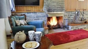 A cozy living room with a stone fireplace, a television mounted on the wall, and a comfortable seating area with a red rug.