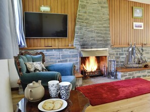 A cozy living room with a stone fireplace, a television mounted on the wall, and a comfortable seating area with a red rug.