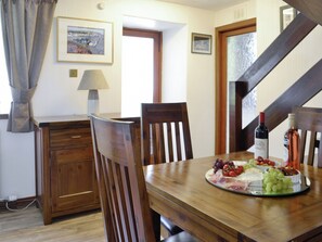A dining area with a wooden table set for a meal, featuring a cheese platter and wine bottles.