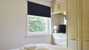 A bedroom with a bed, a window with a view of trees, a dresser, and a lamp.