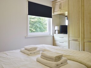 A bedroom with a bed, a window with a view of trees, a dresser, and a lamp.