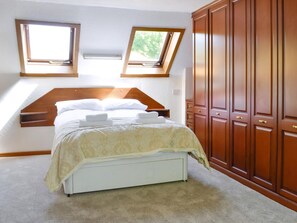 A bedroom with a bed, two skylights, and wooden wardrobe.