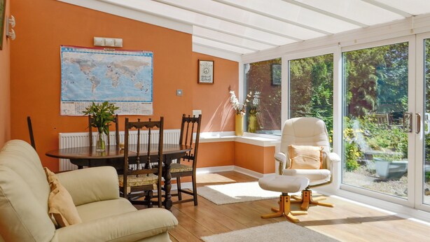 A living room with a sofa, a dining table with chairs, a globe map on the wall, and a view of the outdoors through large windows.
