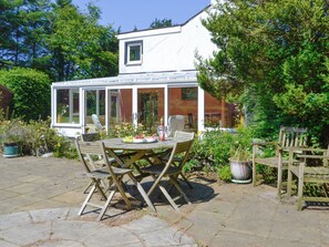 A conservatory with a table and chairs set up for dining, surrounded by lush greenery.