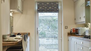 A small kitchen with a dining area, a stone wall outside, and a door leading to a garden. - 2 bedroom accommodation in Bamford, near Hope Valley (Bamford, near Hope Valley)