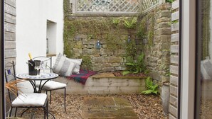 A small, enclosed outdoor space with a stone wall, a wooden bench, a table with chairs, and a bottle of champagne. - 2 bedroom accommodation in Bamford, near Hope Valley (Bamford, near Hope Valley)