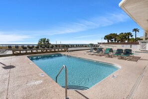 Relax by the rectangular pool surrounded by a sandy deck and lounge chairs with cushions.