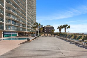 Une promenade en bois avec une piscine, des chaises longues et un bâtiment doté de balcons.