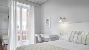 A hotel room with a large bed, a desk, and a chair. There is a window with curtains, a wall-mounted light, and a framed picture. - Always Easy I Escolta Real (San Sebastián/Donostia)