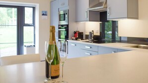 A modern kitchen with a large island, stainless steel appliances, and a bottle of Veuve Clicquot champagne. - The Garden Room at Eudon George (Eudon George, near Bridgnorth)